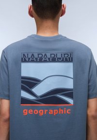 Graphite blue t-shirt with a rectangular graphic featuring stylized waves in light blue and navy, labeled with "NAPAPIJRI" and "geographic" in orange.
