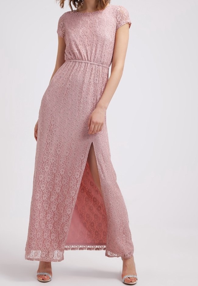 Femme portant une robe longue en dentelle rose, manches courtes, taille cintrée et fente latérale, associée à des talons argentés à bout ouvert.