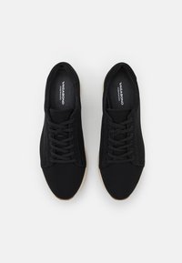 Baskets en toile noire avec une forme arrondie, dotées de lacets noirs, d'une tige en textile et d'une semelle en caoutchouc marron clair.