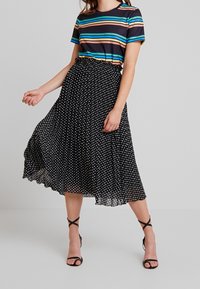 Top de manga corta a rayas con líneas azules, naranjas y blancas, combinado con una falda midi plisada negra con lunares y tacones negros de tiras.