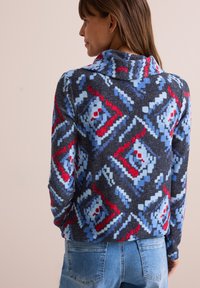 Maglione lavorato a maglia caratterizzato da un motivo geometrico multicolore in tonalità di rosso, blu e grigio, con colletto ripiegato e maniche lunghe.