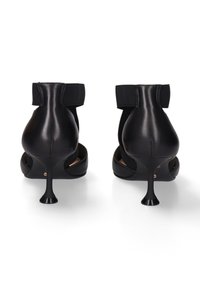 Zwarte leren hakken met een spitse neus, hoge stilettohak en elastische enkelriem. Kenmerkt zich door een gladde afwerking en open zijkanten.