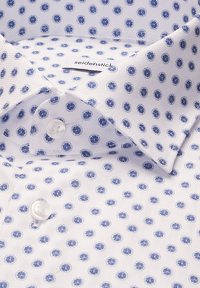 Chemise blanche à pois circulaires bleus, col boutonné, et étiquette de marque visible portant l'inscription "seidenstick".