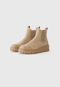 Bottines en cuir beige avec des panneaux latéraux élastiques, bout rond et semelle plateforme épaisse avec des stries horizontales.
