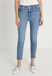 Blå denim jeans med hög midja och smal passform, diskret blekning, femficksdesign och kontrasterande sömmar. Matchas med vita klackskor.