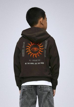 Haut à capuche marron avec un grand design de soleil orange comportant un œil au centre, accompagné de texte. Tissu en coton, coupe décontractée, poche kangourou.