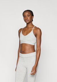 Αθλητικό σουτιέν ανοιχτού γκρι με λεπτές τιράντες και συλλεγμένο μπροστινό μέρος, συνδυασμένο με κολάν ψηλόμεσο που ταιριάζει, με μαλακή και λεία υφή.