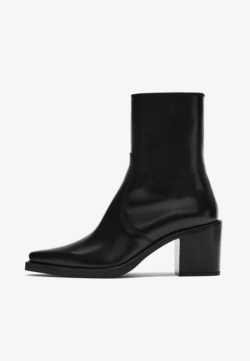 Stivaletto in pelle nera con punta appuntita, design senza cuciture e tacco spesso. Presenta una texture liscia e una silhouette minimalista.