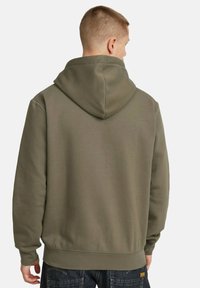 Sudadera verde oliva con una gran capucha, textura suave, puños y dobladillo acanalados, y un corte relajado, vista desde la parte de atrás.
