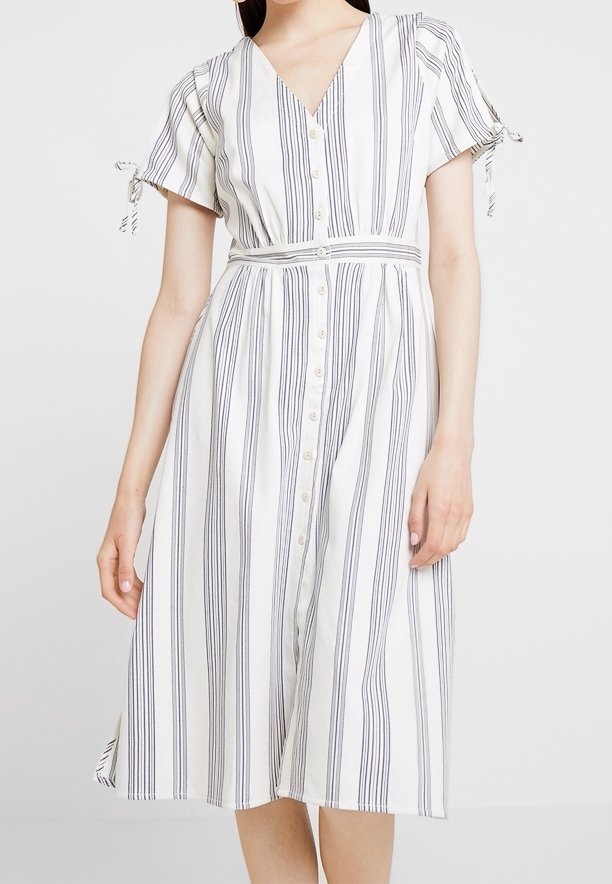 Knäppklänning i knä längd med V-hals, korta ärmar och knytningar. Tillverkad av lätt tyg med vertikala blå ränder på en vit bakgrund.