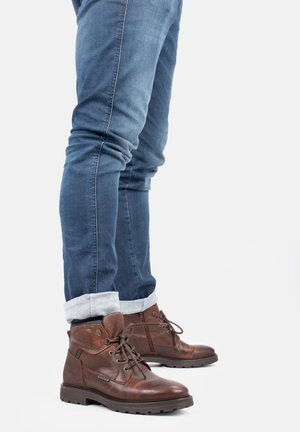 Botas de cuero marrón con un collar acolchado, puntera redonda y diseño de cordones. Combinadas con jeans de mezclilla azul de corte ajustado, con los puños enrollados en los tobillos.