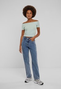 Lysegrønn av skuldrene topp, blå høytlivede rette jeans, og grå joggesko med hvite detaljer. Glatt stoff og ledig passform.
