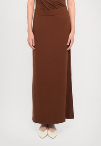 Hnedá maxi sukňa vyrobená z mäkkého materiálu, s hladkým povrchom a bočným rozparkom. V kombinácii s off-white špicatými topánkami.
