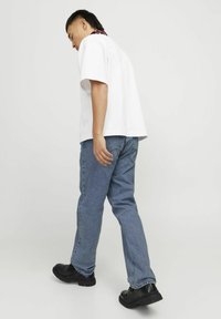 Hvit t-skjorte med korte ermer kombinert med blå denimjeans, med en avslappet passform og svarte sko, sett fra siden.