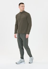 Vihreä urheilullinen puolivetoketjullinen paita, jossa on teksturoitu muotoilu, yhdistettynä samanvärisiin kapeisiin housuihin ja harmaisiin juoksukenkään.