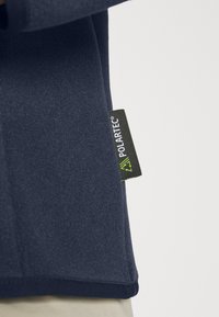 Pullover in pile blu navy con superficie testurizzata, dotato di un'etichetta Polartec verde e nera sul lato e orlo aderente.