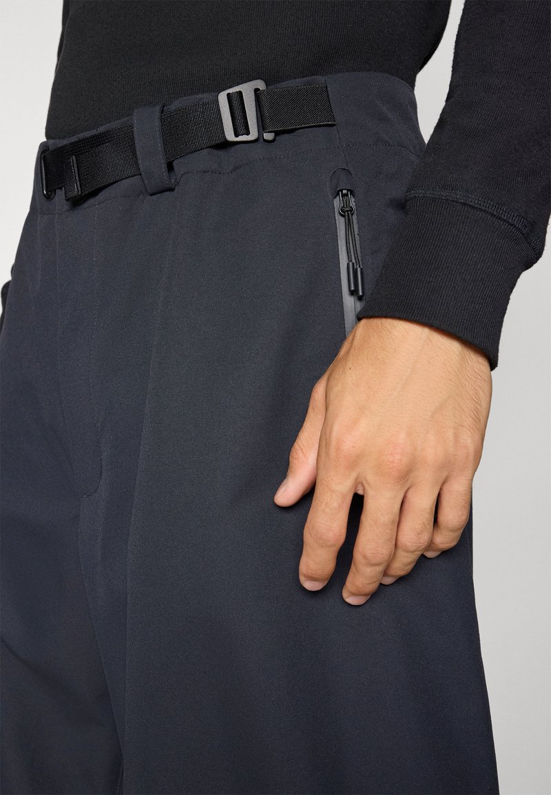 Black, lightweight, stretch fabric trousers feature a fitted waist with an adjustable belt and zippered side pockets. Smooth texture.