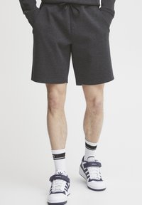 Mørk grå, knelang shorts laget av mykt stoff, med elastisk midjebånd og snøring. Kombinert med hvite sokker og sneakers.
