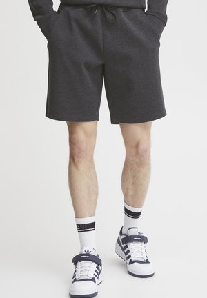 Mørkegrå, knælange shorts lavet af blødt stof, med elastisk talje og snor i taljen. Sammen med hvide sokker og sneakers.