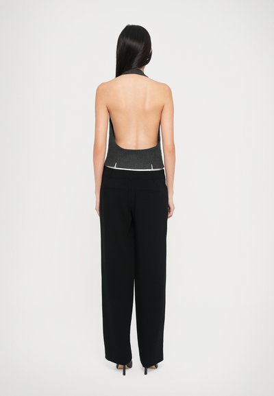 Vue arrière d'une femme portant un top gris à nervures sans manches et à dos nu, associé à un pantalon large noir et des talons pointus.