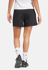 Pantalones cortos deportivos negros con un acabado de tela suave, con una cintura elástica. Combinados con calcetines blancos y zapatillas de running negras.