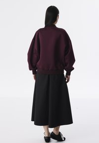 Sudadera oversized color marrón con cuello y puños acanalados, combinada con una falda larga negra. El conjunto presenta un ajuste relajado y una textura suave.