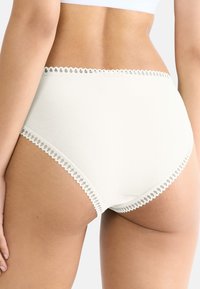 Mutande a vita alta color crema con bordo in pizzo intorno alla cintura e alle aperture delle gambe, realizzate in morbido cotone per il massimo comfort.