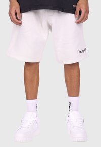 Hvide bomulds shorts med sidesøm, med "Dropside" trykt i sort. Båret med hvide sneakers og hvide ribbede sokker.