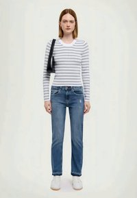 Pilkos ir baltos juostelės ilgarankovė palaidinė, derinama su vidutinio mėlynumo džinsais su nusidėvėjimo detalėmis. Baltos sportbačiai ir juoda kuprinė.