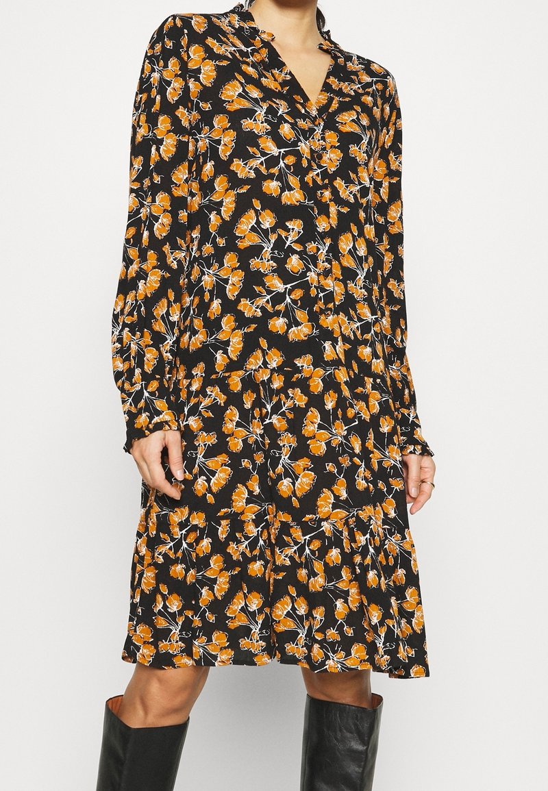 Schwarzes Blumenkleid mit orange- und weißen Blumenmustern, langen Ärmeln, Knopfkragen und rüschenbesäumtem Saum. Hergestellt aus leichtem Stoff.