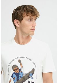 Hvid bomuld t-shirt med et farverigt grafisk motiv af en skateboarder. Rund halsudskæring og korte ærmer.