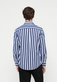 Μακρυμάνικη μπλούζα με ναυτικό μπλε και λευκές κατακόρυφες ρίγες, βαμβακερό υλικό, κλασικό γιακά, κουμπωτούς καρπούς και καμπυλωτή ραφή στο κάτω μέρος.