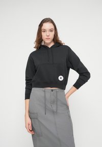 Μαύρο cropped φούτερ με κουκούλα, εμπρόσθια τσέπη και πλακέτα με λογότυπο, συνδυασμένο με γκρι cargo φούστα που έχει πλαϊνές τσέπες και σούρα στη μέση.