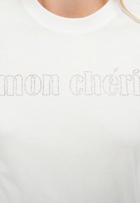 Λευκό βαμβακερό t-shirt με το κείμενο "mon chéri" διακοσμημένο με μικρές ασημένιες στρας. Κλασικό σχέδιο με στρογγυλή λαιμόκοψη.