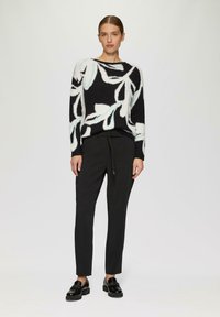 Zwart-wit trui met een blauw bloemenpatroon, gecombineerd met zwarte taps toelopende broek en glanzende zwarte schoenen. Casual outfit met textuur.