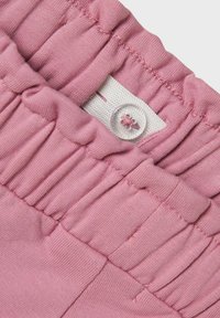 Tela de algodón rosa con detalle de fruncido en la cintura, que presenta un cierre de botón único. Textura suave con un ajuste blando y flexible.