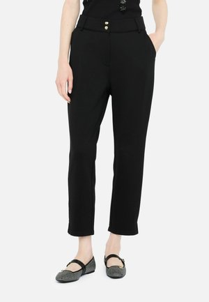 Pantaloni neri su misura in tessuto elasticizzato, con vita piatta, due tasche frontali e dettagli in bottone dorato. Indossati con ballerine a fantasia.