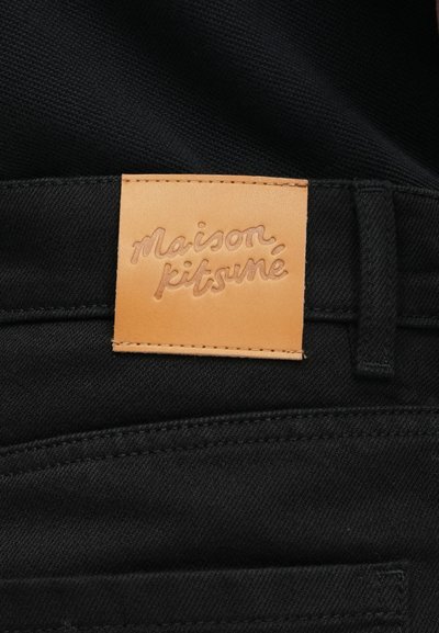 Juodos audinio džinsai su rudos odos etikete, ant kurios iškilmingai užrašytas "maison kitsuné" logotipas. Švarios linijos ir klasikiniai siuvimo detalės.