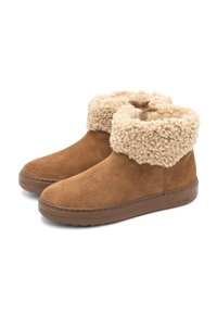 Botas de ante marrón hasta el tobillo con un puño de pelaje sintético texturizado en color crema y suelas de goma, que presentan un ligero tacón para mayor soporte.