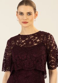 Bordeauxfarbenes Spitzenkleid mit floralen Mustern, kurzen Ärmeln und einem geschichteten Design. Strukturierte Spitzenoberlage mit einer glatten Unterlage.