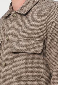 Καφέ σακάκι με σχέδιο, γιακά με περιλαίμιο, διαθέτει μία τσέπη στο στήθος και κλείσιμο με κουμπιά, κατασκευασμένο από υφασμάτινο υλικό με υφή.