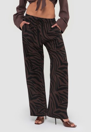 Kvinde iført brune bukser med vide ben og sorte zebrastriber, kombineret med brune hælede sandaler og en kort brun top med lange ærmer.