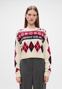 Krém színű crop pulóver piros és tengerészkék gyémántmintákkal és hópihe motívumokkal. Az elülső részen vastag sötétkék betűkkel a "TOMMY GIRL" felirat található.