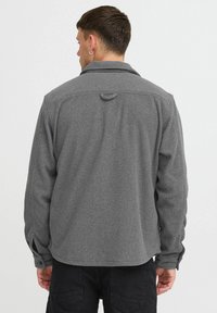 Gray fleece shirt with a collar, long sleeves, and button cuffs; features a loop at the back and a textured finish.