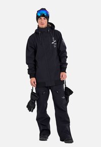 Black snowboarding outfit featuring a zip-up jacket and loose pants, with zippered pockets and gloves, complemented by mirrored goggles.