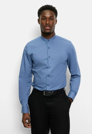 Long-sleeve light blue dress shirt with a stand collar, button-front design, and smooth texture; paired with black pants and belt.