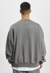 Grå oversized sweatshirt med ribbet tekstur, afslappet pasform og manchetterede ærmer. Har en rund halsudskæring og en let buet kant.