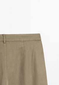 Pantalons en lin de couleur kaki, dotés d'une taille lisse et d'une texture subtile, présentant des coutures piquées et un design épuré.