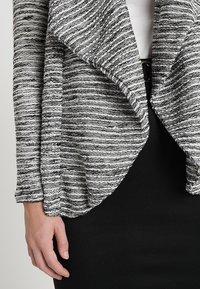 Gray and white striped cardigan with a draped shawl collar, textured fabric, and long sleeves, paired with a black fitted skirt.