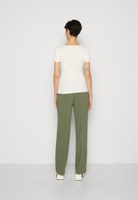 Bílý krátký rukáv top spárovaný s olivově zelenými kalhotami s širokými nohavicemi, které mají hladkou texturu a minimalistický design. Jednoduché pozadí.